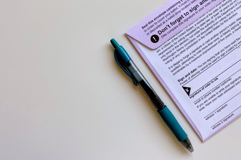 An absentee ballot and a blue pen sitting on a white table.