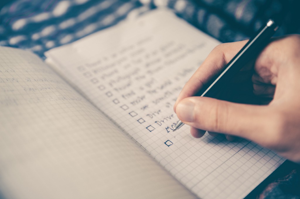 An image of a notebook with several checkboxes and a person holding a pen.