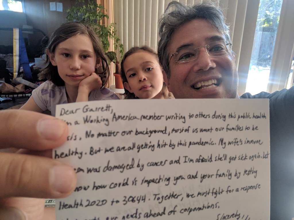 An image of a man smiling and holding up a letter sitting alongside his two children.
