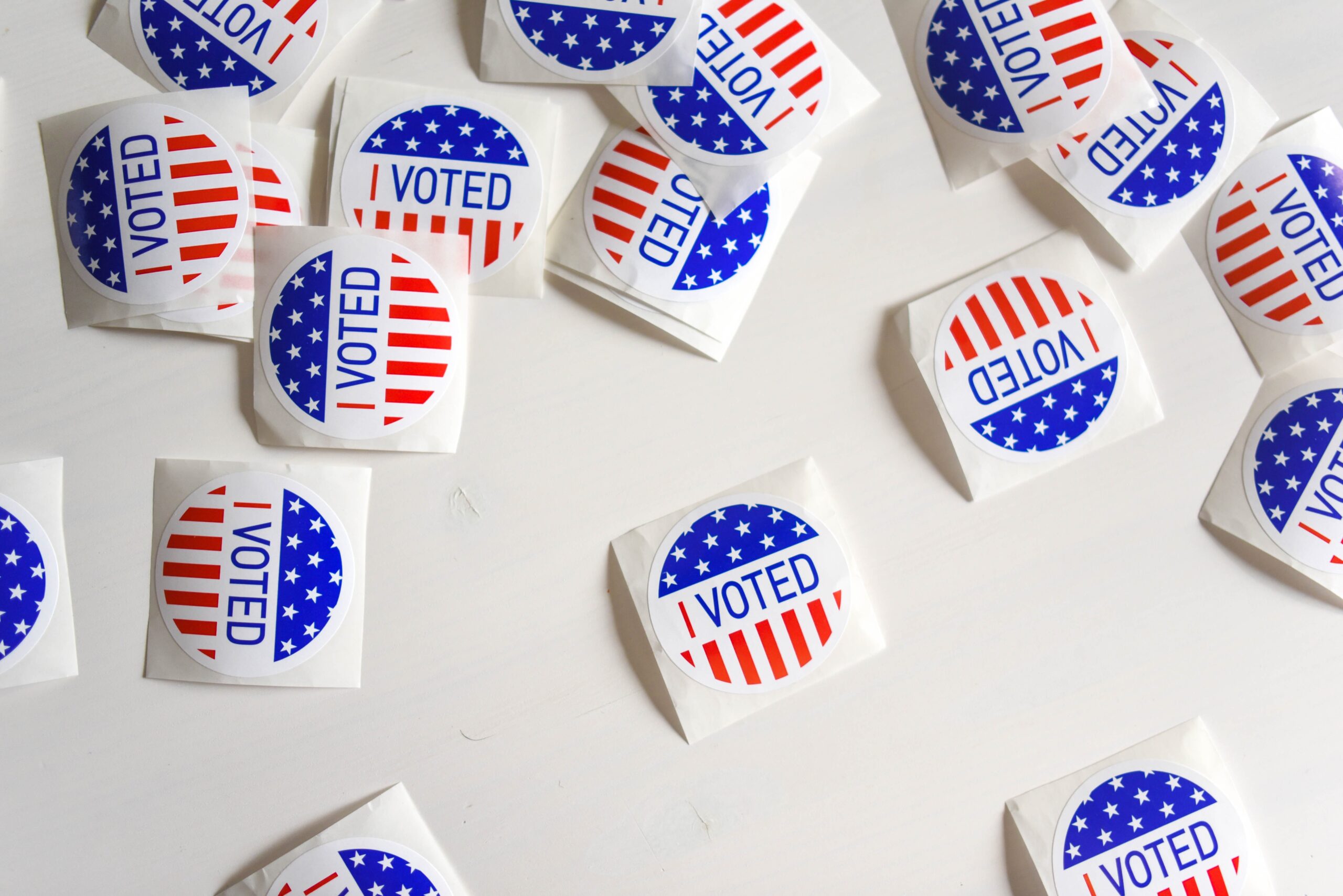 Red, white, and blue "I VOTED" stickers lying on a white surface.