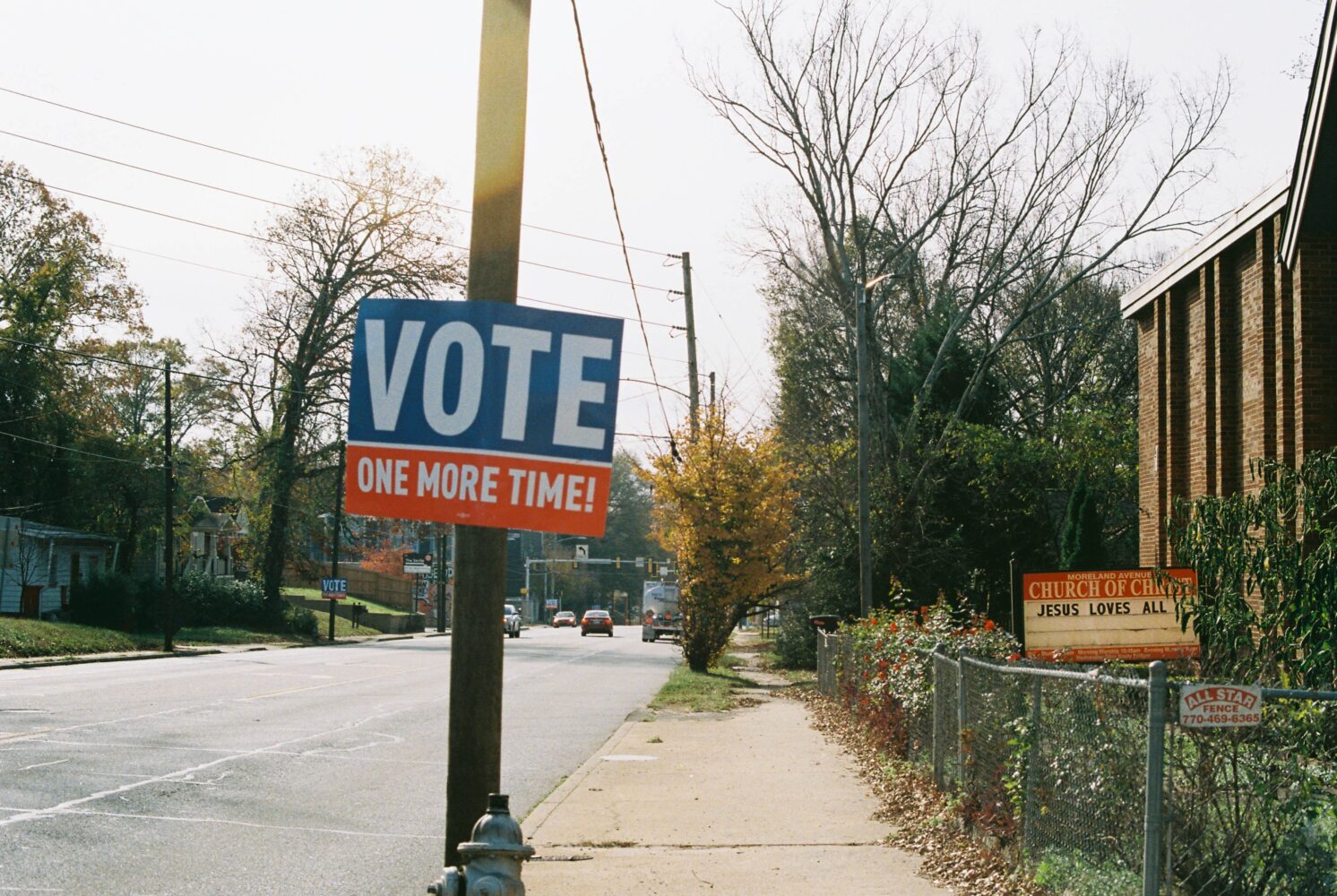 A photo of a sidewalk and a telephone poll with a sign that reads "VOTE. One more time."