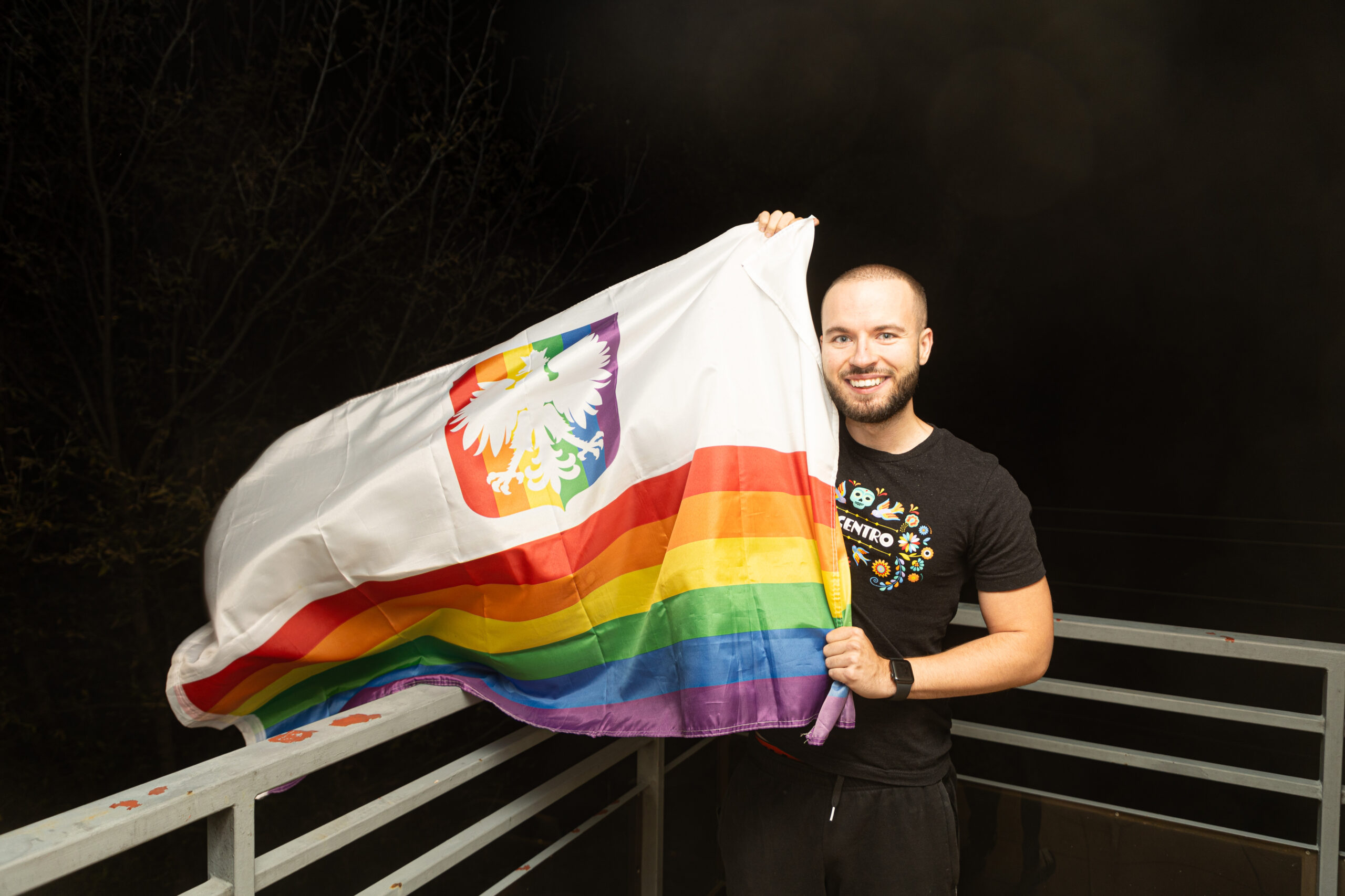 Polish LGBT+ activist Bart Staszewski holds up a Polish pride flag and smiles