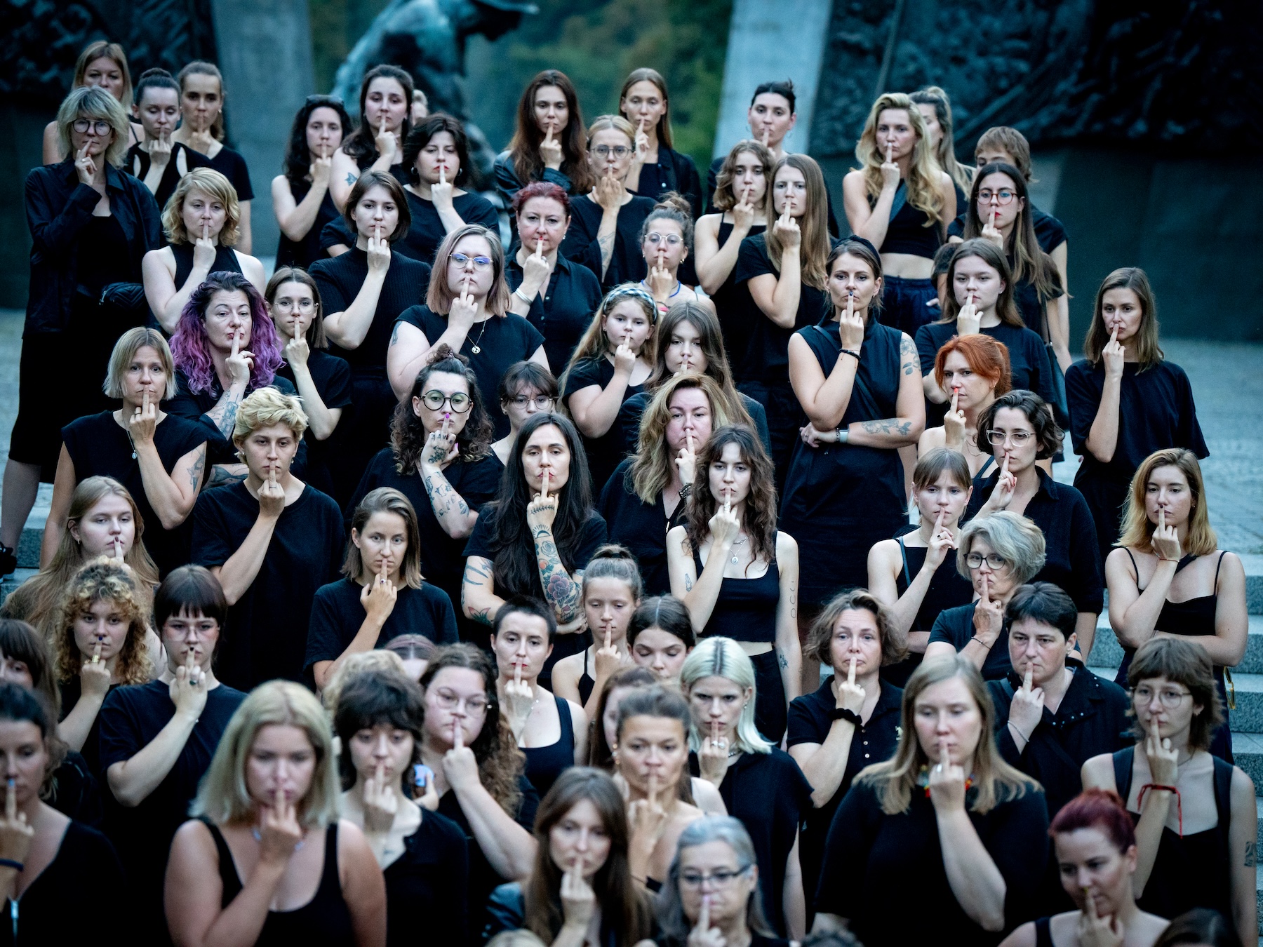 A group of women wearing black holding their middle fingers over their mouths in protest