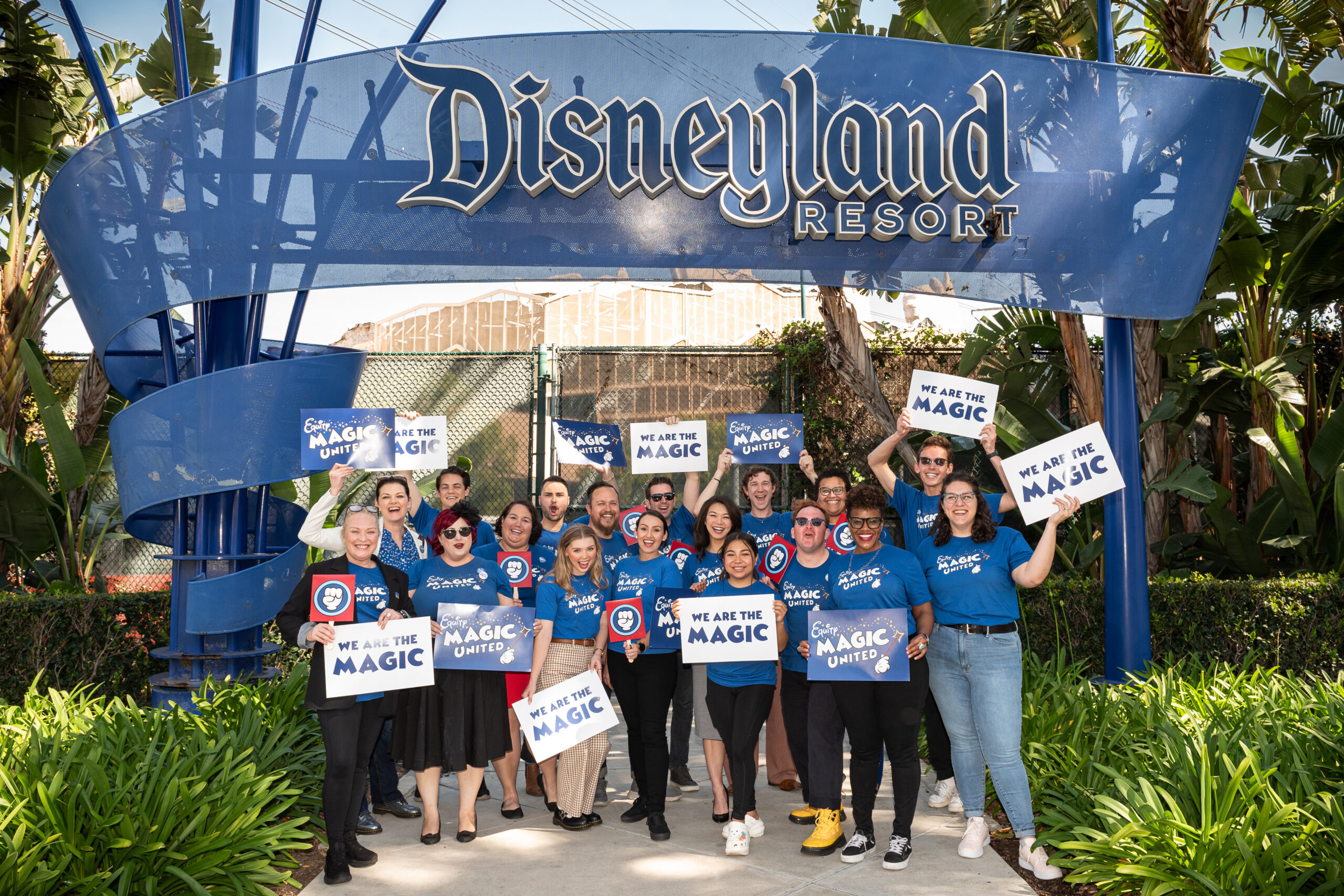 Staff of Actors' Equity with Cast Members of Magic United posing in front of the Disneyland Resort sign holding signs that say "We Are The Magic".