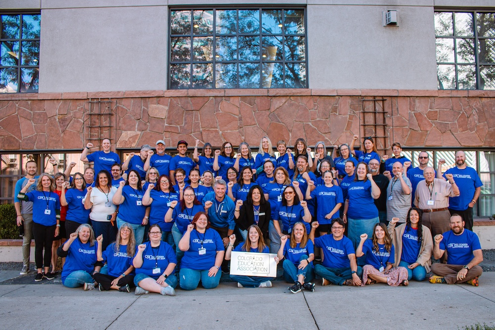 A group of people wearing matching blue CEA shirts posing with their fists in the air. A person in the front is holding a sign that says "Colorado Education Association."