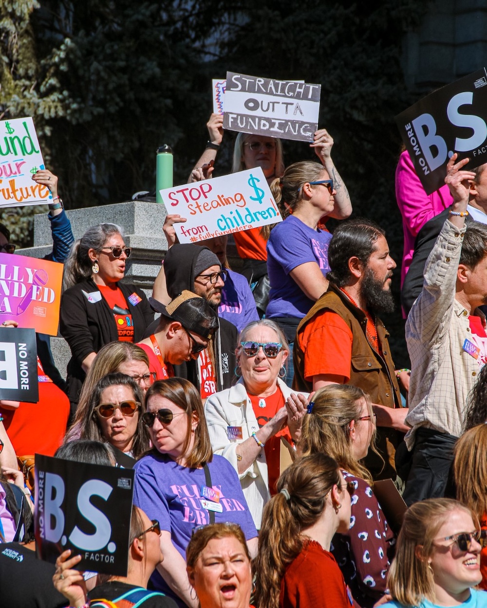 A group of CEA members at a rally holding signs that read, "Stop stealing $ from children", "No more B.S. factor", and others.