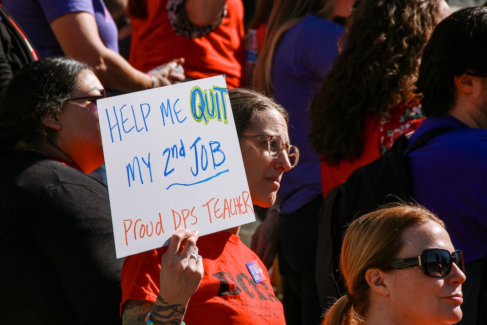 A CEA member at a rally holding a sign that says, "Help me quit my 2nd job — Proud DPS Teacher"