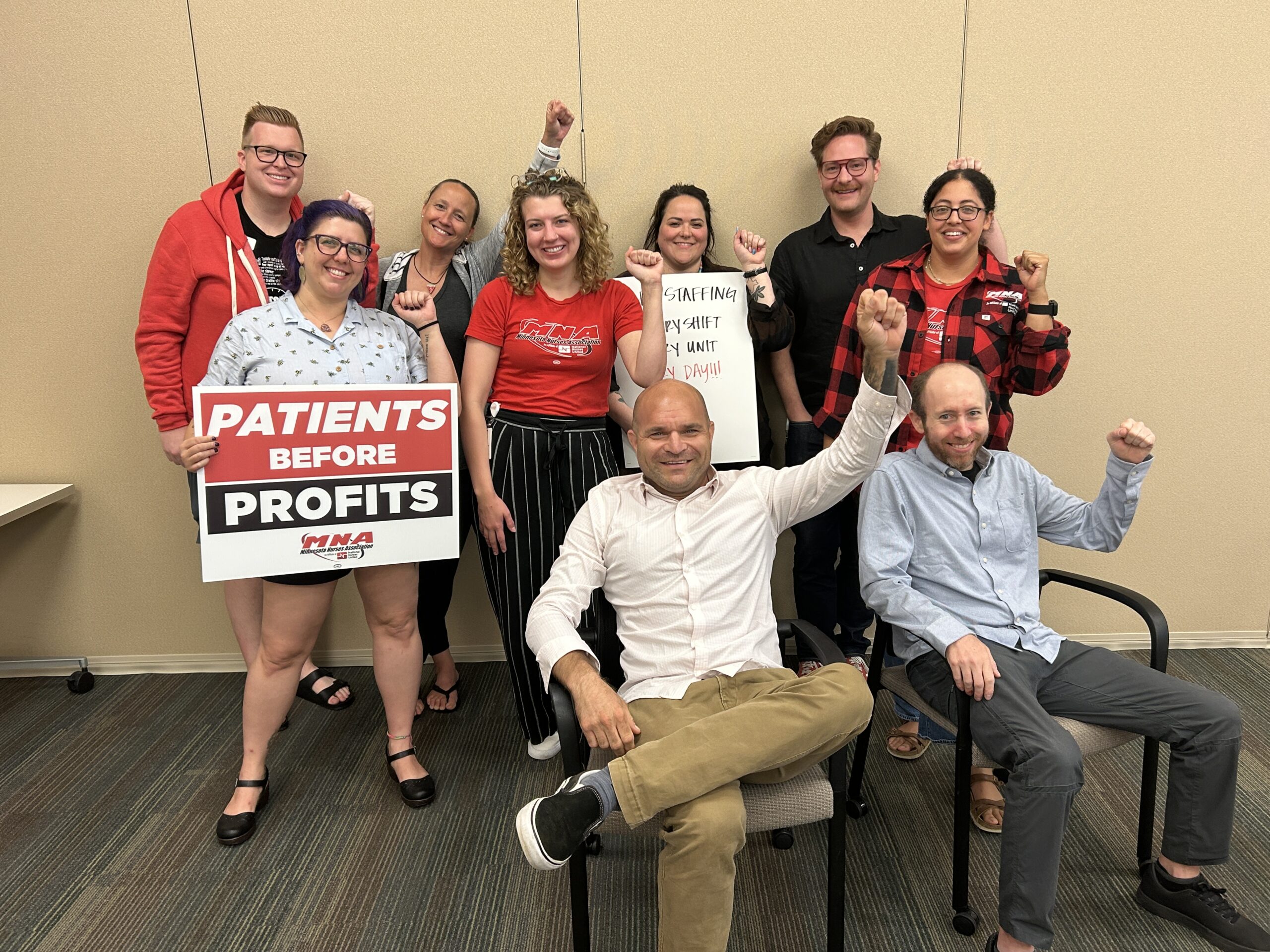 A group of people posing and holding up fists with a sign that reads "Patients Before Profits".