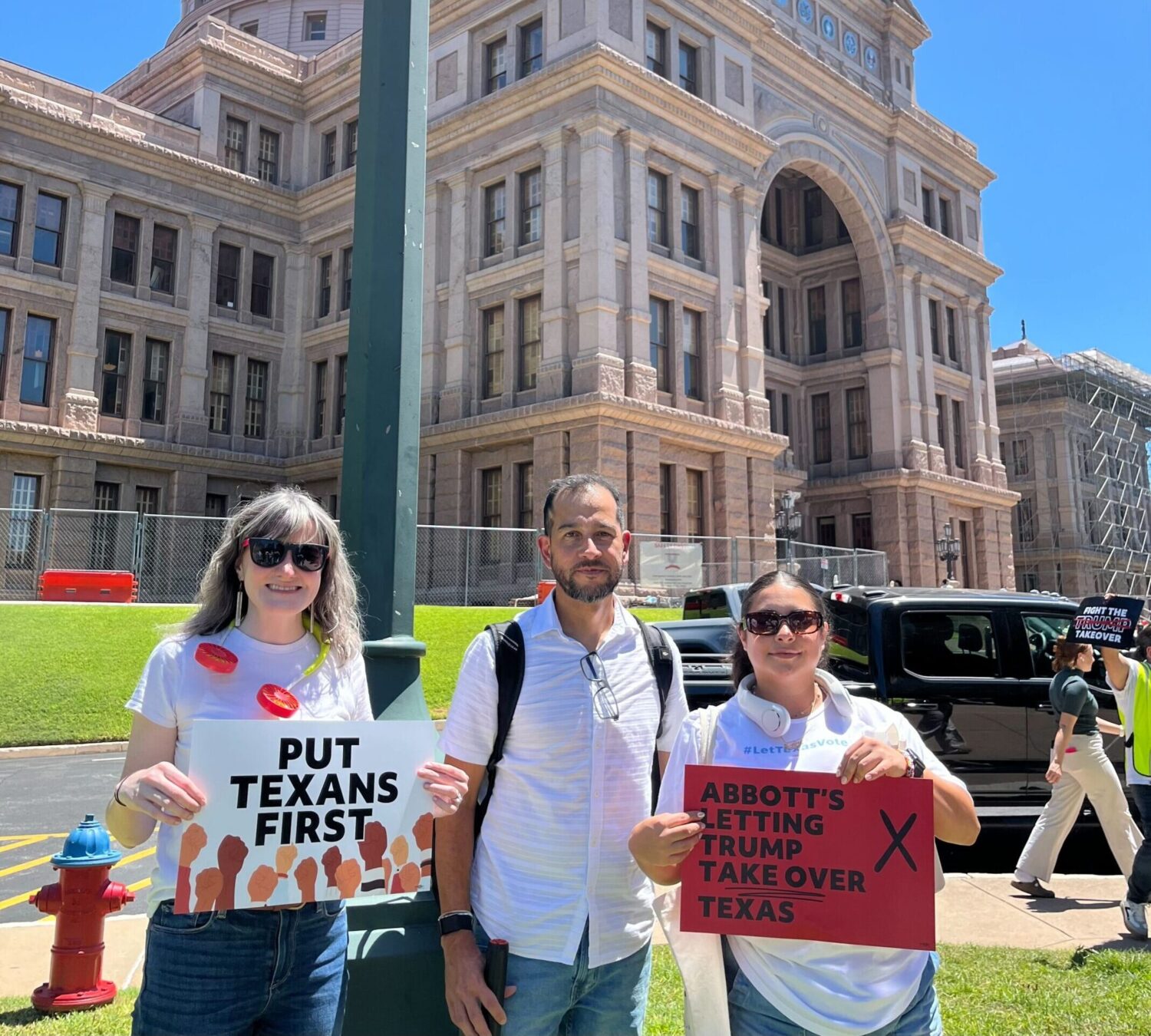 Three Common Cause members hold signs outside of the Texas State House that say "Put Texans First" and "Abbott's letting Trump take over Texas"